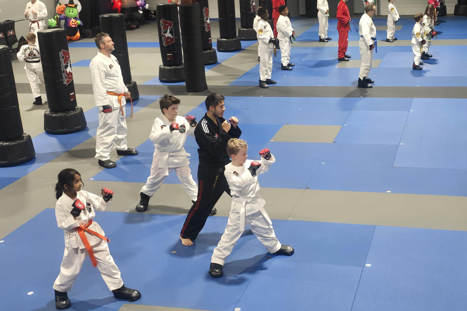 Adults and kids practice fighting stances side by side in sparring gear during an ATA Martial Arts class.