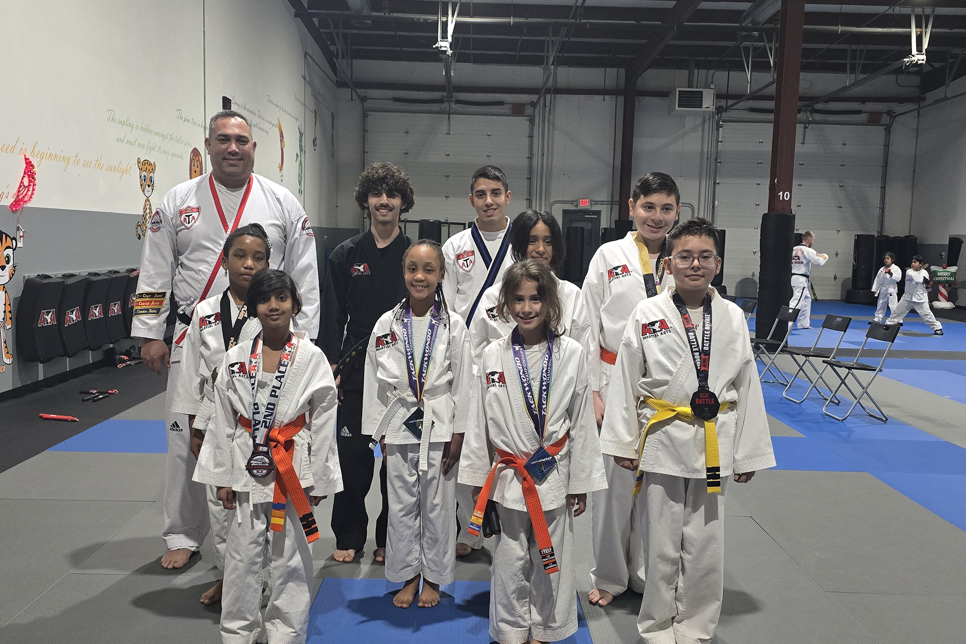 ATA Martial Arts students in uniforms with colored belts pose with tournament medals alongside their instructors in the studio.